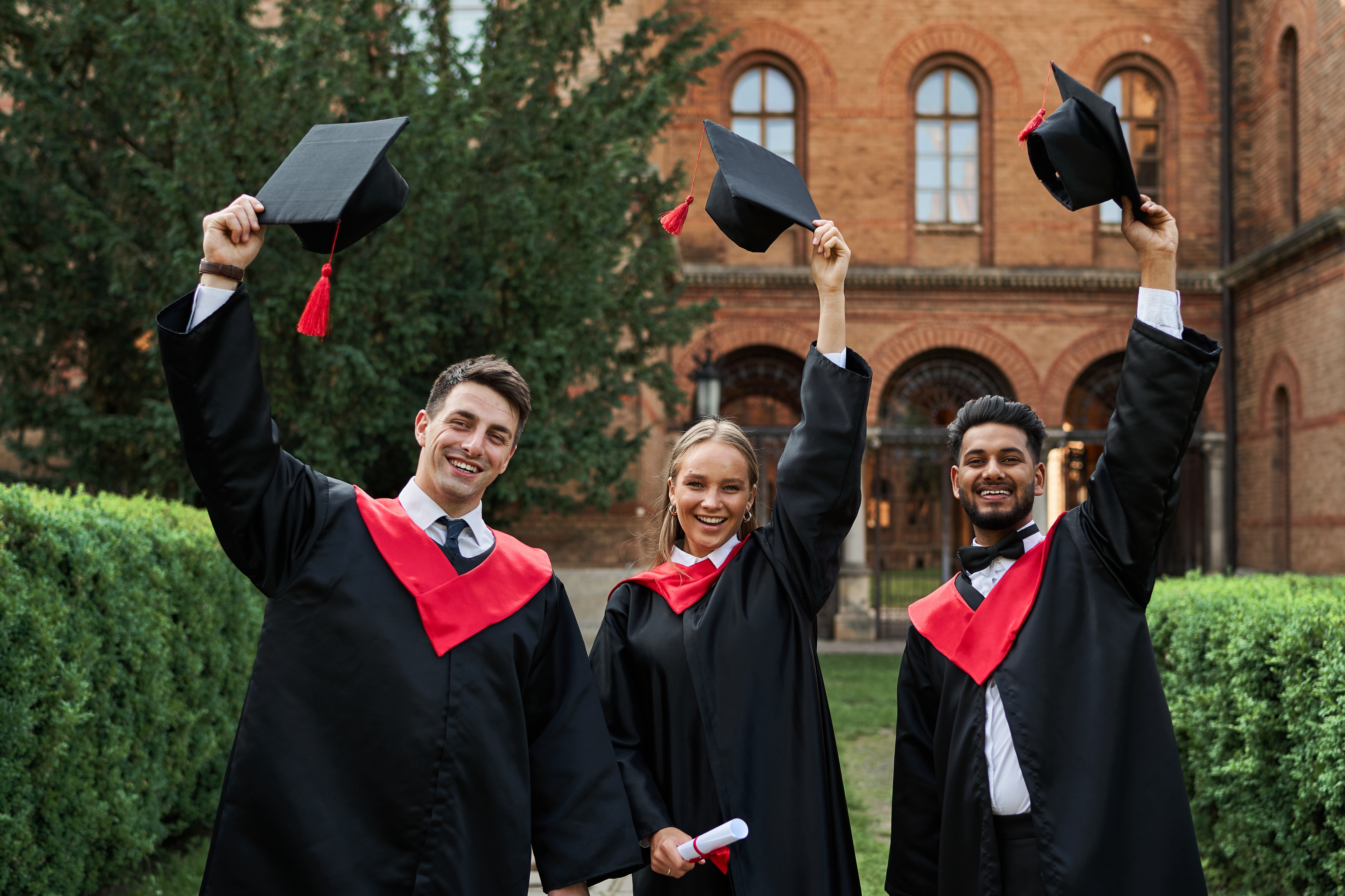 Three triumphant college graduates raise their caps on graduation day.